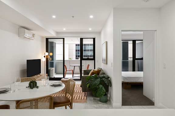 A modern dining room with a table set for two and a view of a balcony outside.