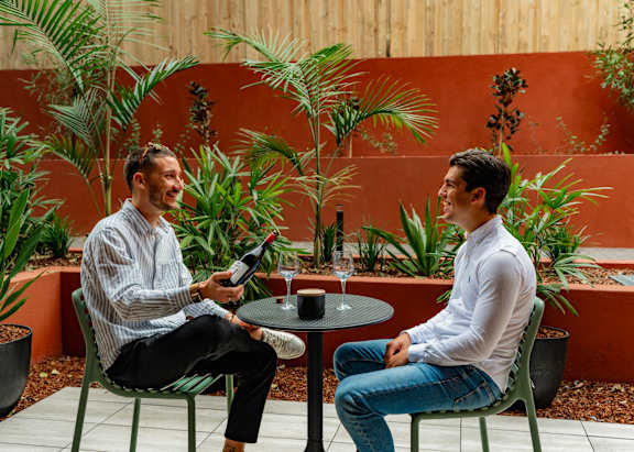 Two men are sitting at a table with a glass of wine and a cup of coffee.