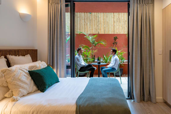 two men sitting at a table in a hotel room with a bed
