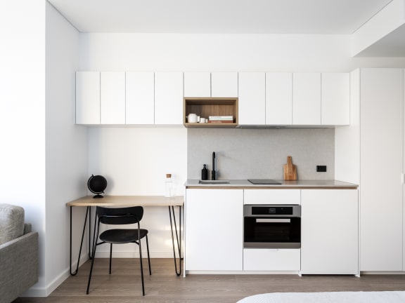 a small kitchen with white cabinets and a desk with a chair