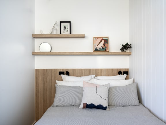 a bedroom with a bed with white pillows and a wooden shelf above it