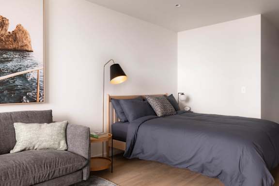 A bedroom with a bed, a couch, and a painting on the wall.