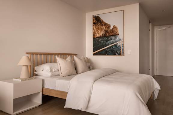A bedroom with a large bed and a picture of a cliff by the sea on the wall.