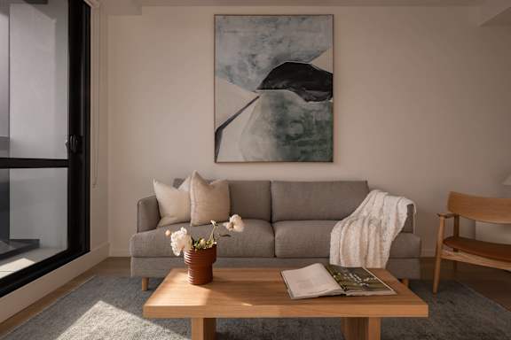 A living room with a grey couch, a wooden table with a vase of flowers, a book, and a magazine.