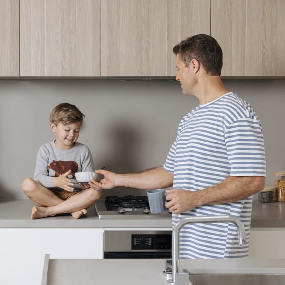 a man holding a cup and a boy sitting on a kitchen counter