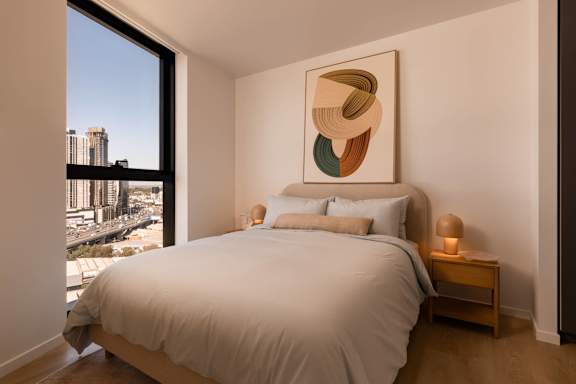 A bedroom with a large bed and a large window overlooking a cityscape.