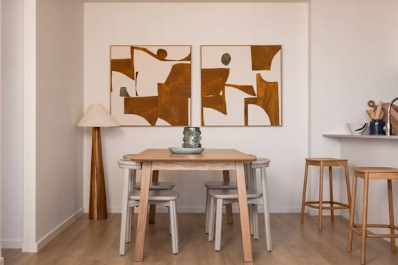 A table with chairs and a lamp in a room with a painting on the wall.