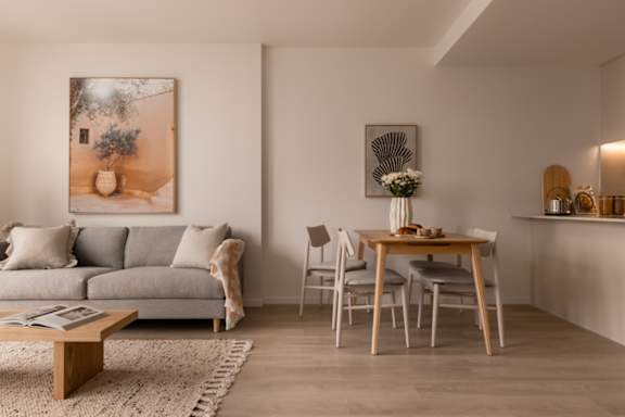 A living room with a grey couch, a coffee table, a dining table with chairs, and a painting on the wall.
