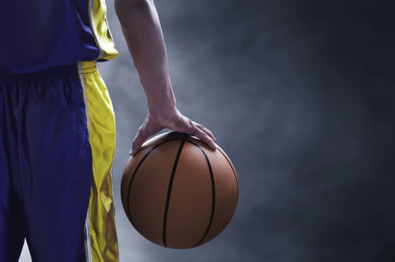 Alt text - Man holding  red colored basket ball in his right hand
