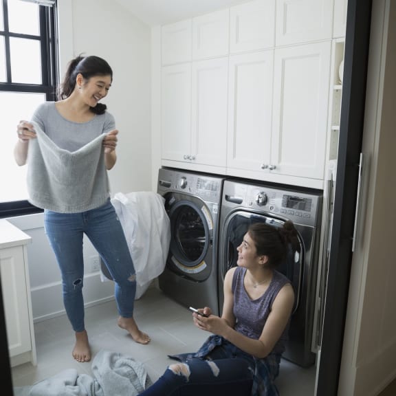 Two young girls enjoying in a layndry roon sitting next to washer and Dryer
