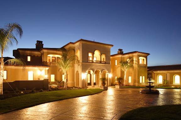A large, well-lit house with a driveway in front.