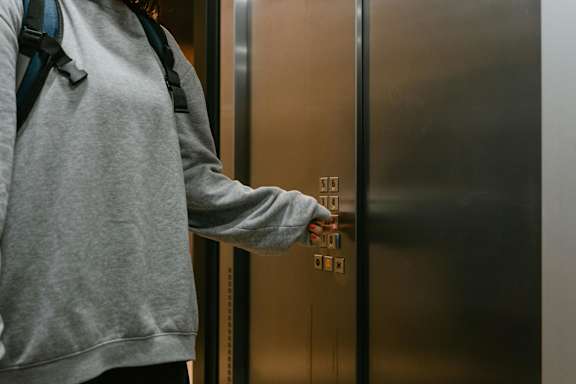 A person in a grey hoodie is pressing a button on an elevator.