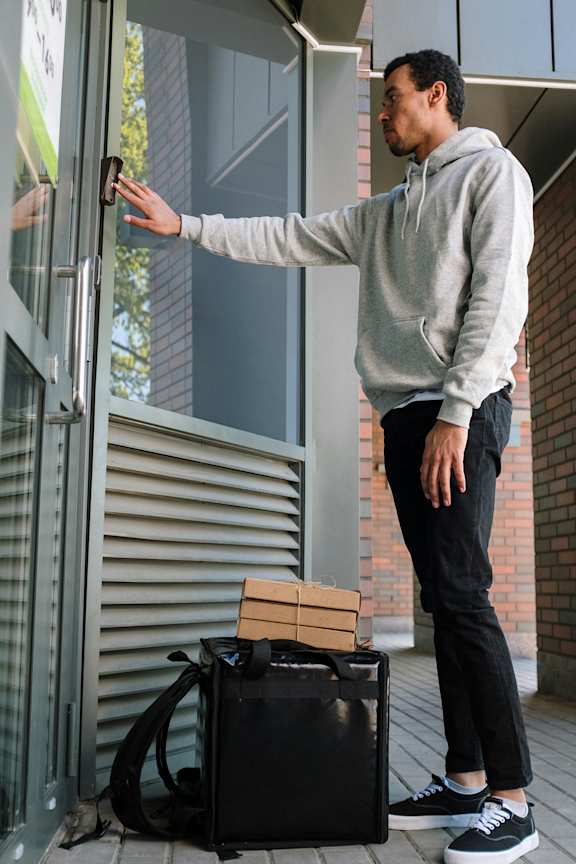 A man in a grey hoodie and black pants is opening a glass door.