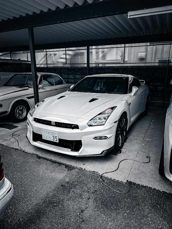 A white Nissan car is parked in a garage.