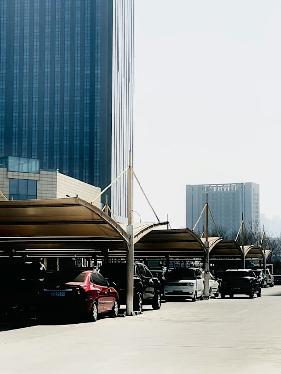 Cars are parked under a canopy in a parking lot.