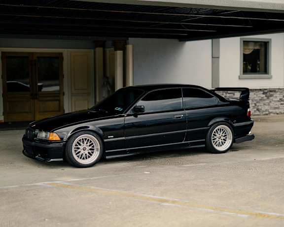 A black car with white rims is parked in front of a building.