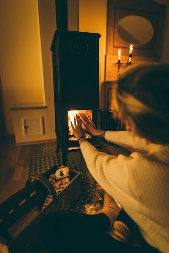 A person is warming their hands by a lit fireplace.