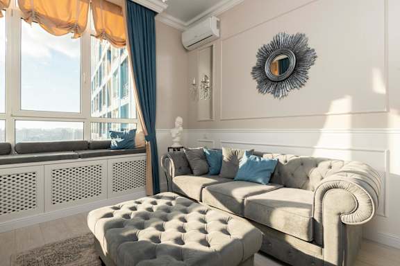 A living room with a grey couch and a round mirror on the wall.