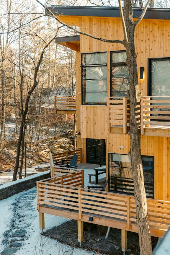 A wooden cabin with a balcony and a tree in front.
