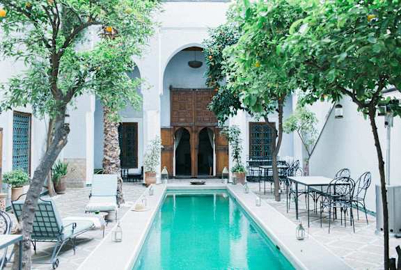 A pool in the middle of a patio with chairs and trees.