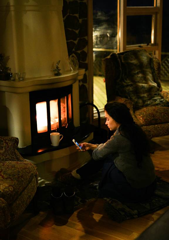 A woman sitting on the floor in front of a lit fireplace.