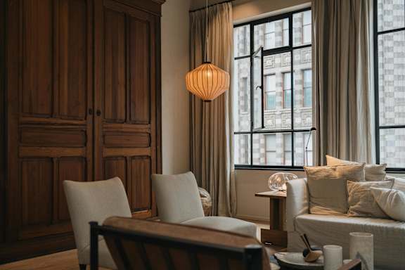 A room with a wooden cabinet, a chair, a table, and a window with curtains.