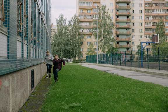 Two people are running on a grassy area in front of apartment buildings.