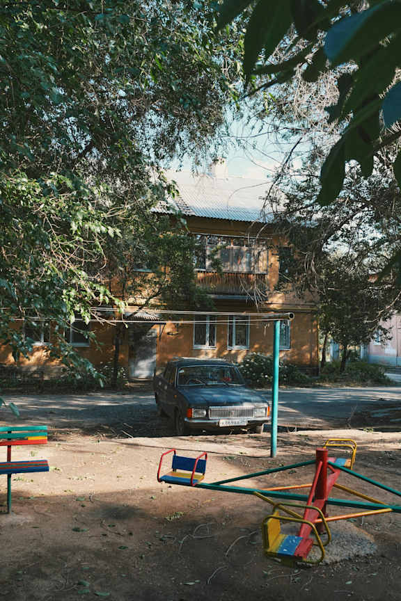 A playground with a swing set and a car parked in front of a house.