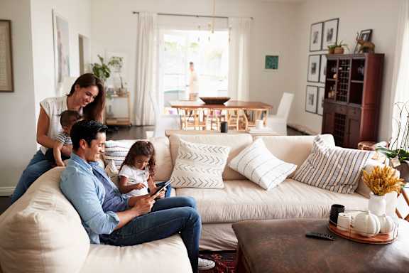 A family of three is sitting on a white couch in a living room.