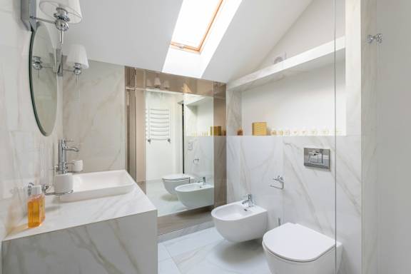 A white bathroom with a marble counter top and a skylight.