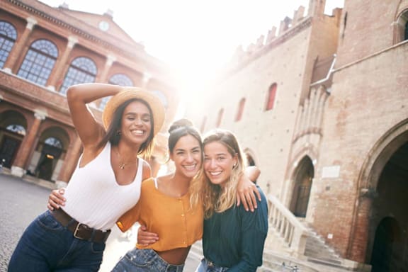 Three women are standing in front of a building with a castle-like appearance.