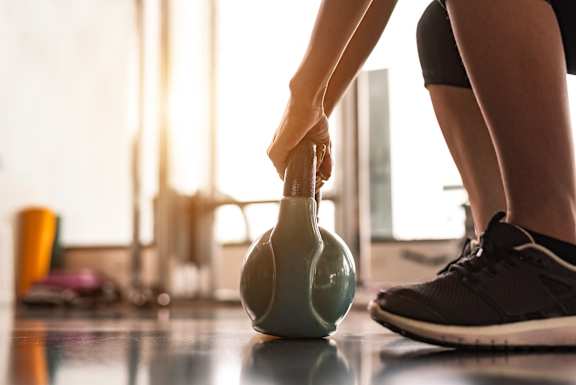 A person is holding a kettlebell while standing on a tiled floor.