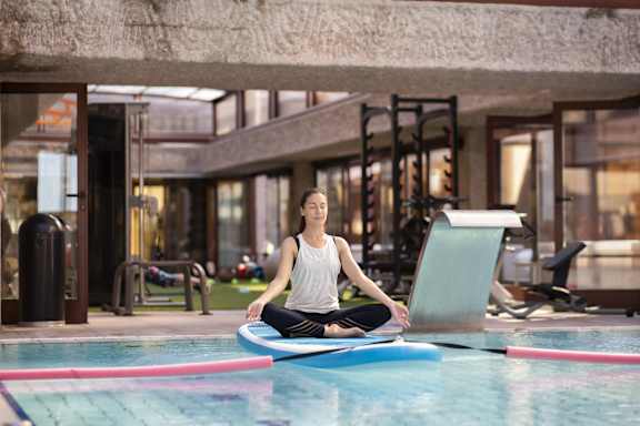 A woman is sitting on a floating mat in a pool.
