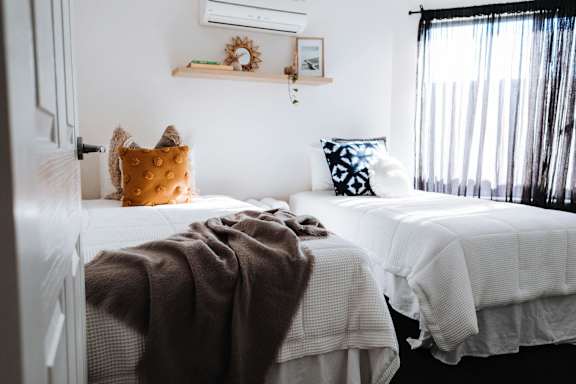 Two beds with white bedspreads and pillows in a room.