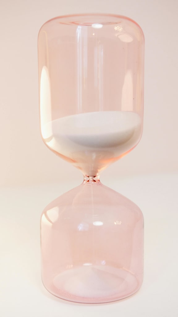 A pink hourglass with white sand in the middle.