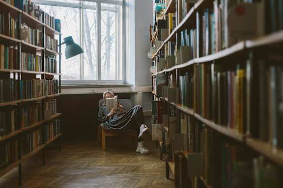 A person is sitting on a chair in a library, reading a book.