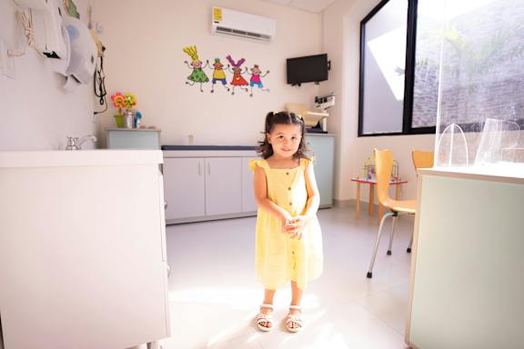 A little girl in a yellow dress stands in a brightly lit room.