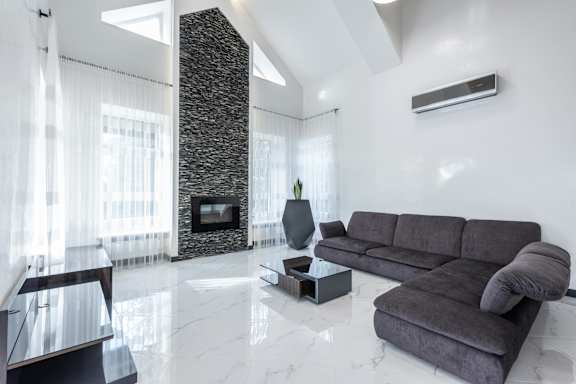 A grey couch sits in a white room with a stone pillar and a fireplace.