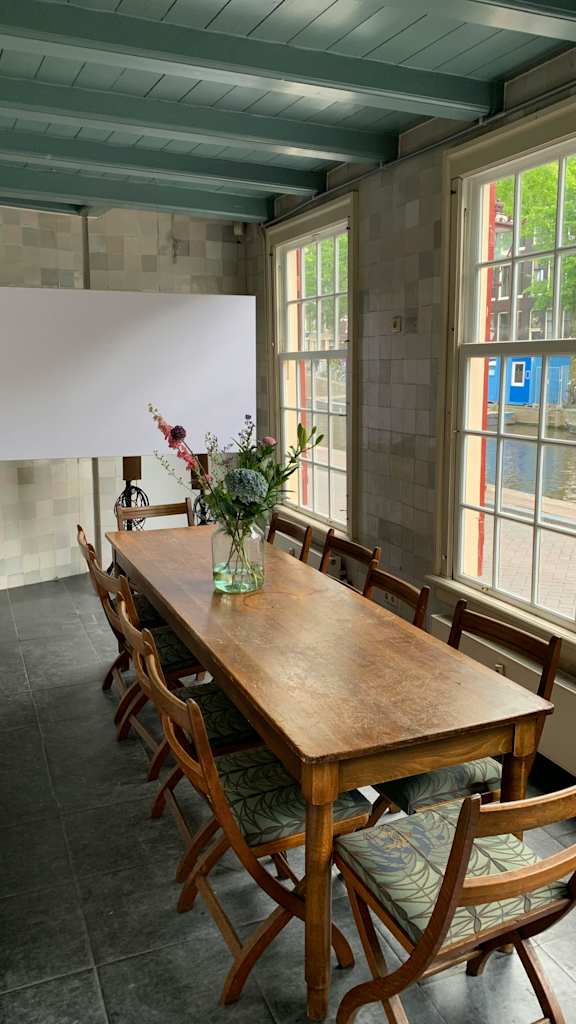 A long wooden table with chairs around it and a vase of flowers on the table.