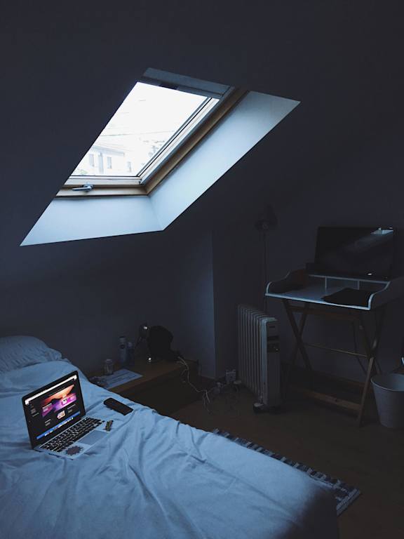 A laptop is open and turned on, placed on a bed in a dimly lit room.