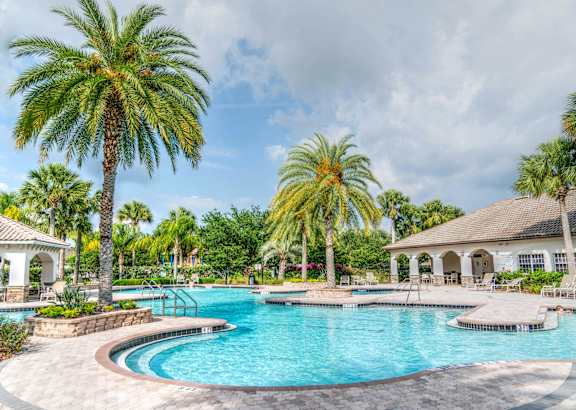 A swimming pool surrounded by palm trees and a gazebo.