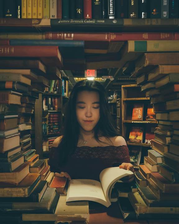 A woman is reading a book in a room full of books.