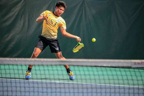 A man in a yellow shirt and black shorts playing tennis.
