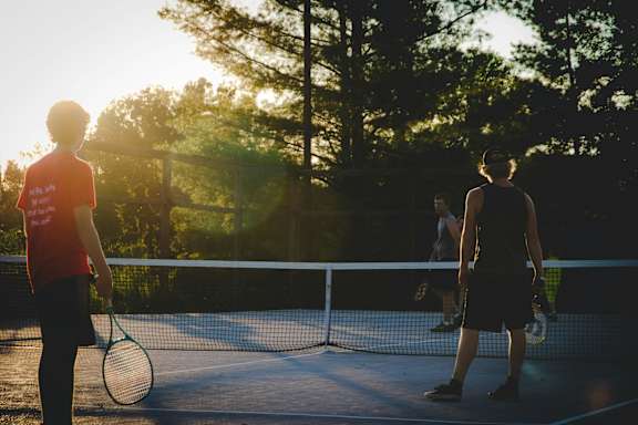 Two people playing tennis on a court with trees in the background.