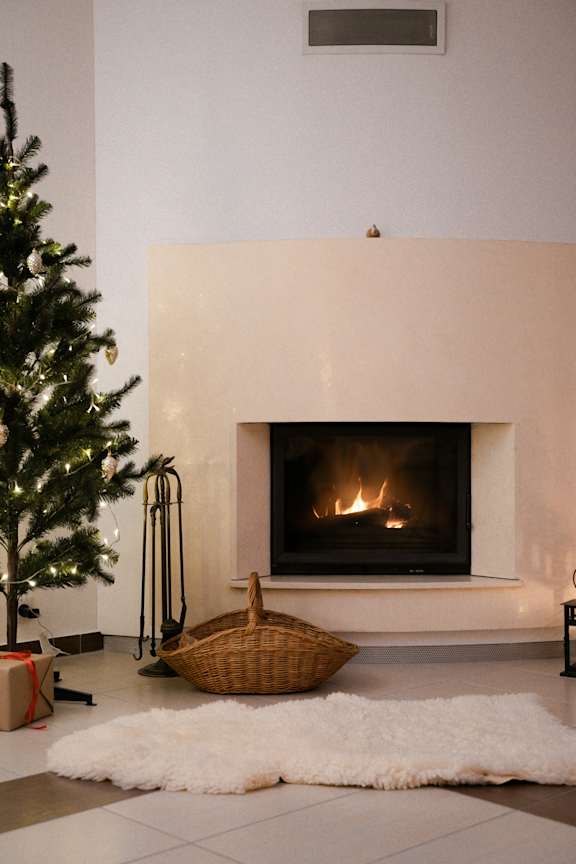 A Christmas tree stands next to a lit fireplace in a modern room.