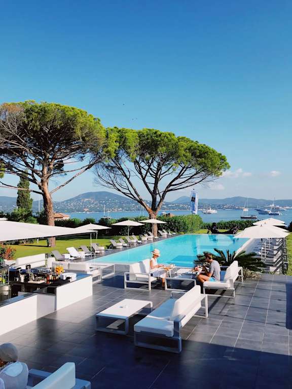 A poolside area with people relaxing and trees in the background.