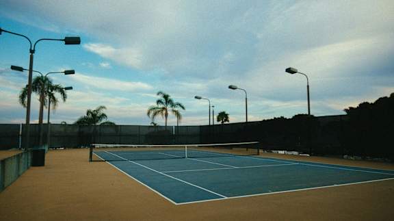 A tennis court with a net and light poles.