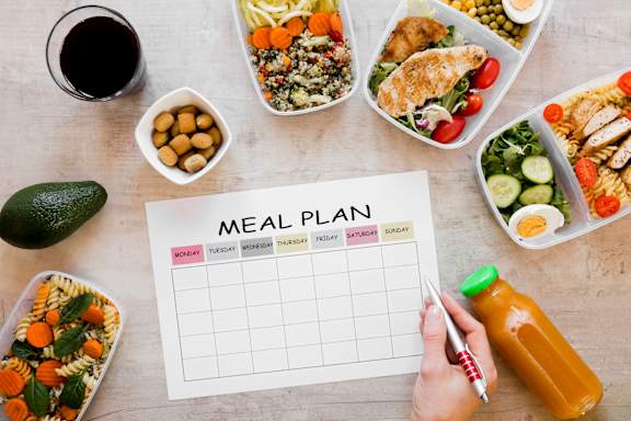 A meal plan is displayed on a table with various healthy foods and a glass of wine.