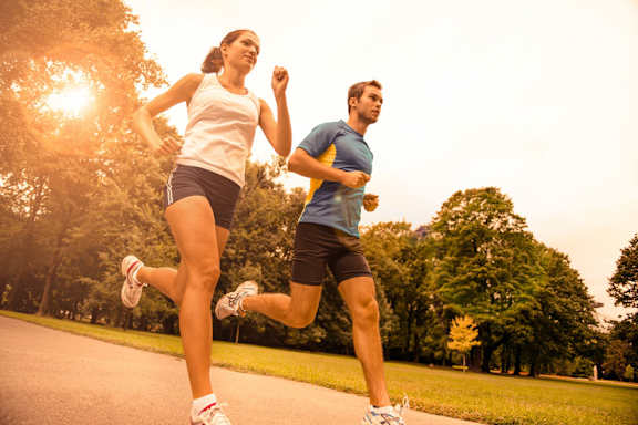 A man and a woman are running on a road in a park.