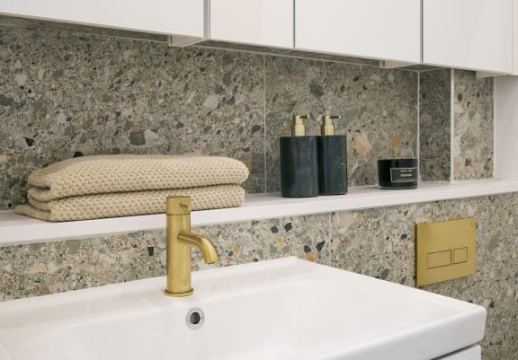 a white sink with a gold faucet and a shelf with towels and other bathroom items
